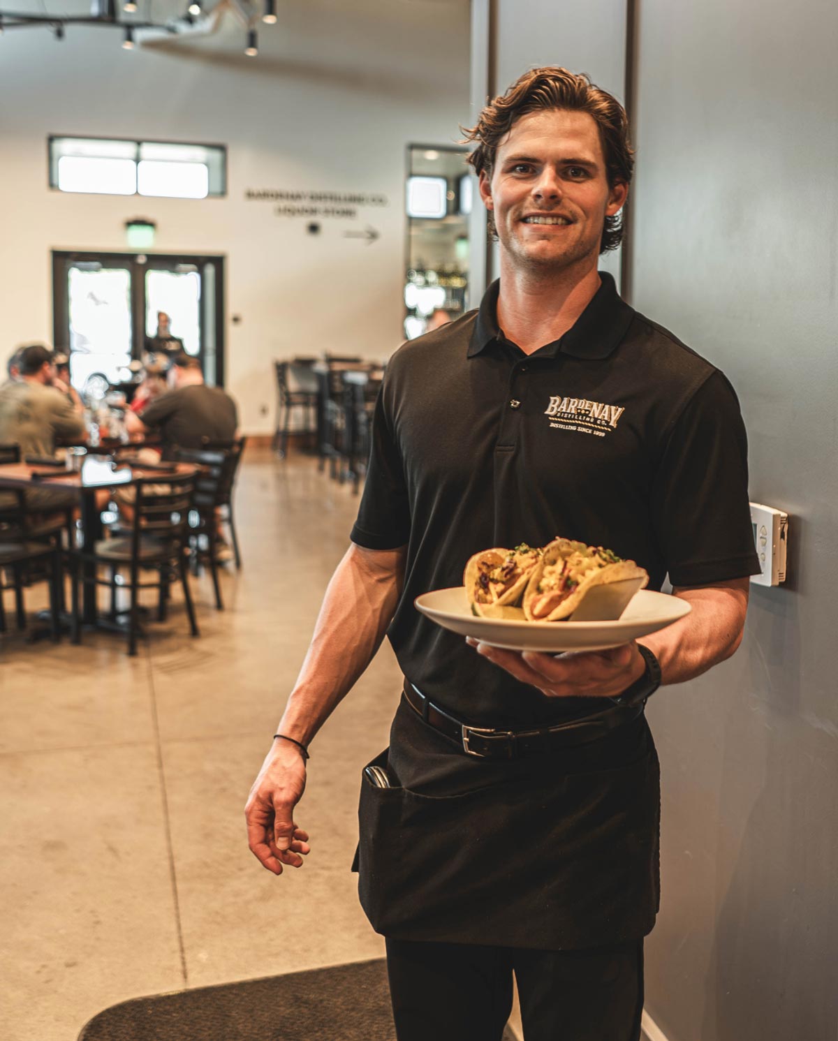 Smiling Bardenay employee holding a delicious plate of tacos.